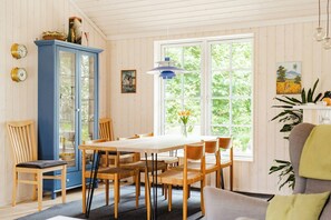 A dining area with a wooden table and chairs, a blue cabinet, and a window with a view of greenery. - Home among trees with architectural flair (Dronningmølle)