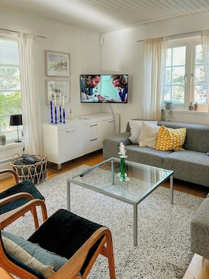 A living room with a sofa, a glass coffee table, a TV mounted on the wall, and a wicker basket. - House with forest and beachside location in Åhus (Åhus)