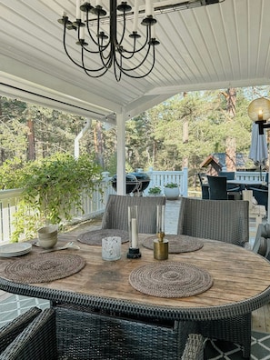 An outdoor patio with wicker furniture, a table set with candles, and a view of trees and a building in the background. - House with forest and beachside location in Åhus (Åhus)