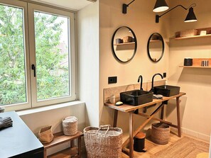 Ein modernes Badezimmer mit Fenster, zwei Spiegeln, einem Waschbecken und einem Holztisch.