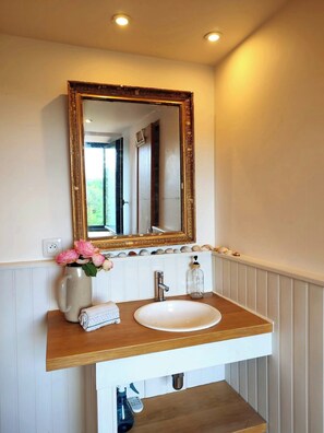A bathroom with a wooden vanity, a white sink, a gold-framed mirror, a vase with flowers, and a bottle of soap. - Charming renovated workshop in Ardèche (Joyeuse)