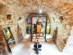 A room with a stone wall, a ceiling fan, a mounted exercise machine, and a poster on the wall. - Charming renovated workshop in Ardèche (Joyeuse)