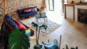 A stone-walled room with a sofa, a small table, and a kitchen area. - Charming renovated workshop in Ardèche (Joyeuse)