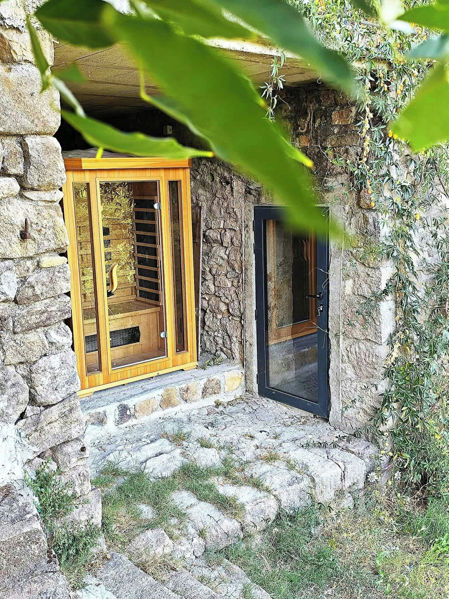 A stone building with a wooden door and window, surrounded by greenery.