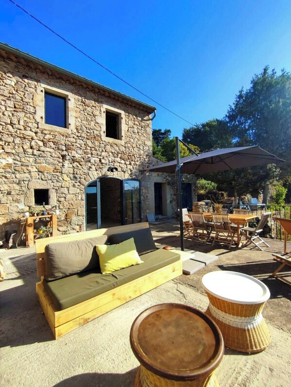A stone building with a sofa and outdoor furniture, including a table and chairs. - Charming renovated workshop in Ardèche (Joyeuse)