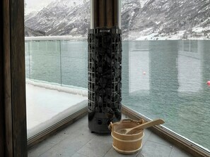 Una habitación con un amplio ventanal con vistas a un lago, una chimenea y un cubo de madera.