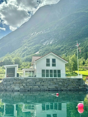 Una casa con un muro in pietra, una bandiera e una montagna sullo sfondo.