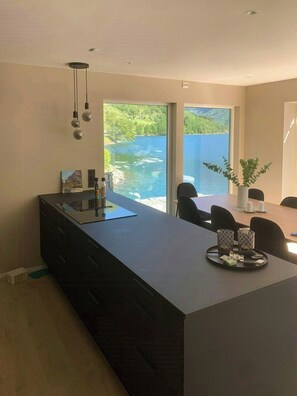Una cucina moderna con una grande isola, un'area pranzo con sedie e vista su un lago attraverso ampie finestre.