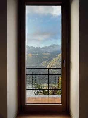 A door leading to a balcony with a view of a mountainous landscape.