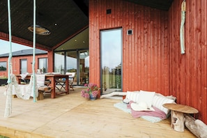 Eine Holzterrasse mit Tisch, Stühlen und einer Hängematte sowie einem Baumstamm-Tisch.