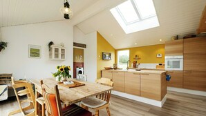 A spacious kitchen with wooden cabinets, a central island, and a dining area with a wooden table and chairs. - Family house with sauna near Ålbæk (Ålbæk)