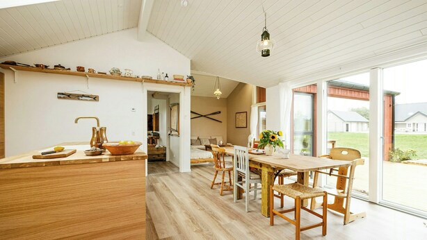 A spacious kitchen with wooden countertops, a dining area with a large table and chairs, and a view of the outdoors through large windows. - Family house with sauna near Ålbæk (Ålbæk)