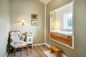 Ein Zimmer mit einem Bett, einem Sessel, einem Nachttisch, einer Lampe und einem Spiegel, der das Bett reflektiert.