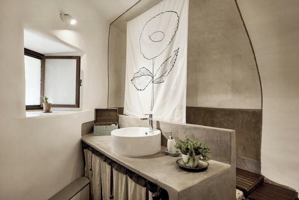 Ein Badezimmer mit einem runden Waschbecken, einem Handtuchhalter, einer Topfpflanze und einem Fenster mit Blick.
