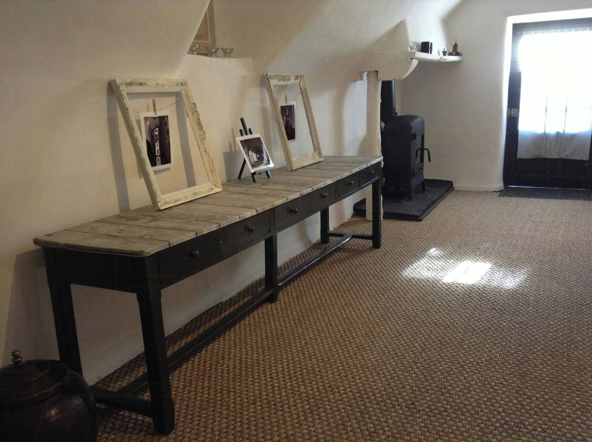 A room with a long wooden bench, framed pictures on the wall, a fireplace, and a carpeted floor.