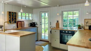 Een keuken met een houten aanrecht, een spoelbak, een fornuis en een raam met uitzicht op groen.