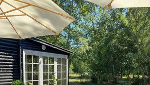 Een houten terras met een tafel, stoelen en een klein huisje met een raam.