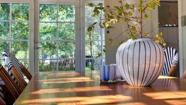 Een houten plafond, een grote vaas met een plant en een tafel met stoelen.