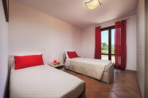 Une chambre avec deux lits, une petite table sur laquelle se trouve un panier de fruits, et une vue sur la verdure par la fenêtre.