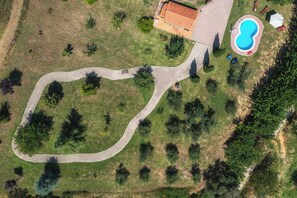 Une vue aérienne d’une propriété avec un chemin sinueux, une piscine et un bâtiment doté d’un toit rouge.