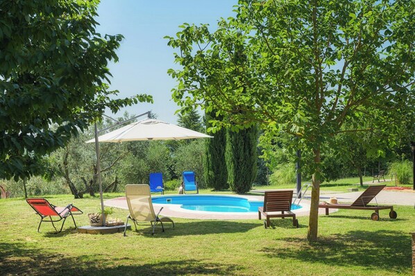 Un espace piscine comprenant des chaises longues, un coin salon abrité et une pelouse bien entretenue.
