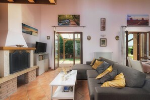 Ein Wohnzimmer mit Fernseher, Kamin, Sofa und Blick auf einen Garten durch Glastüren.