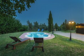 Ein Pool mit einer umlaufenden Liegefläche, zwei Liegestühlen und einem Lampenpfosten.