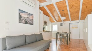 Um interior moderno com um sofá cinzento, piso de madeira, área de refeições e cozinha ao fundo.