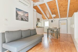 Ein modernes Interieur mit einem grauen Sofa, Holzböden, einem Essbereich und einer Küche im Hintergrund.