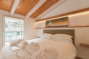 Ein Hotelzimmer mit Bett, Handtüchern, einem Bild eines Segelboots und einem Balkon mit einem Sessel.