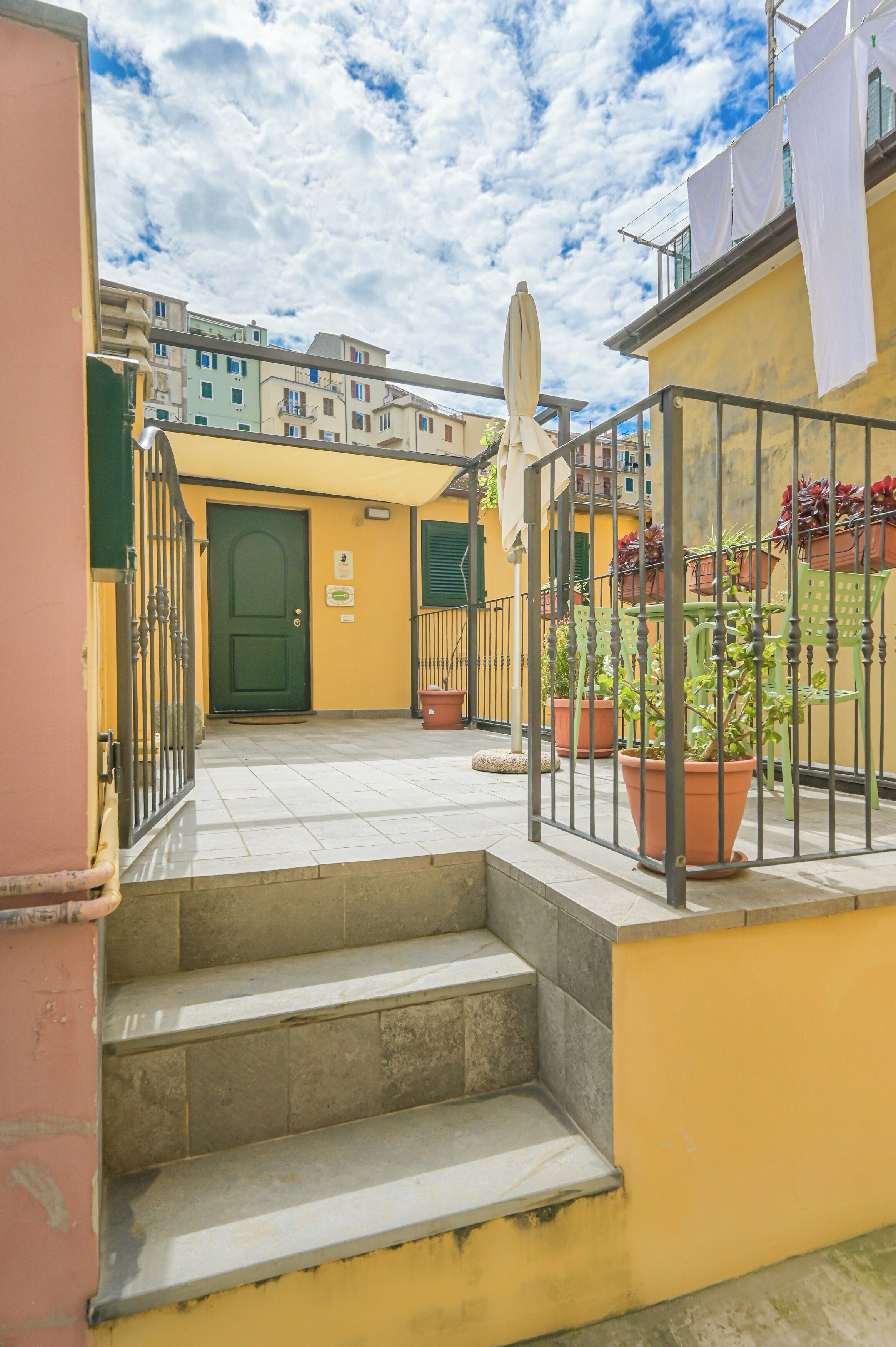 A courtyard with steps leading to a door, potted plants, and a railing.