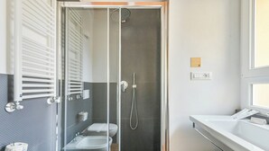 Casa de banho moderna com cabine de duche de vidro, duas lavatórios, sanita e porta-toalhas.