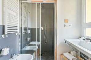 Ein modernes Badezimmer mit Duschkabine, zwei Waschbecken, Toilette und Handtuchhalter.