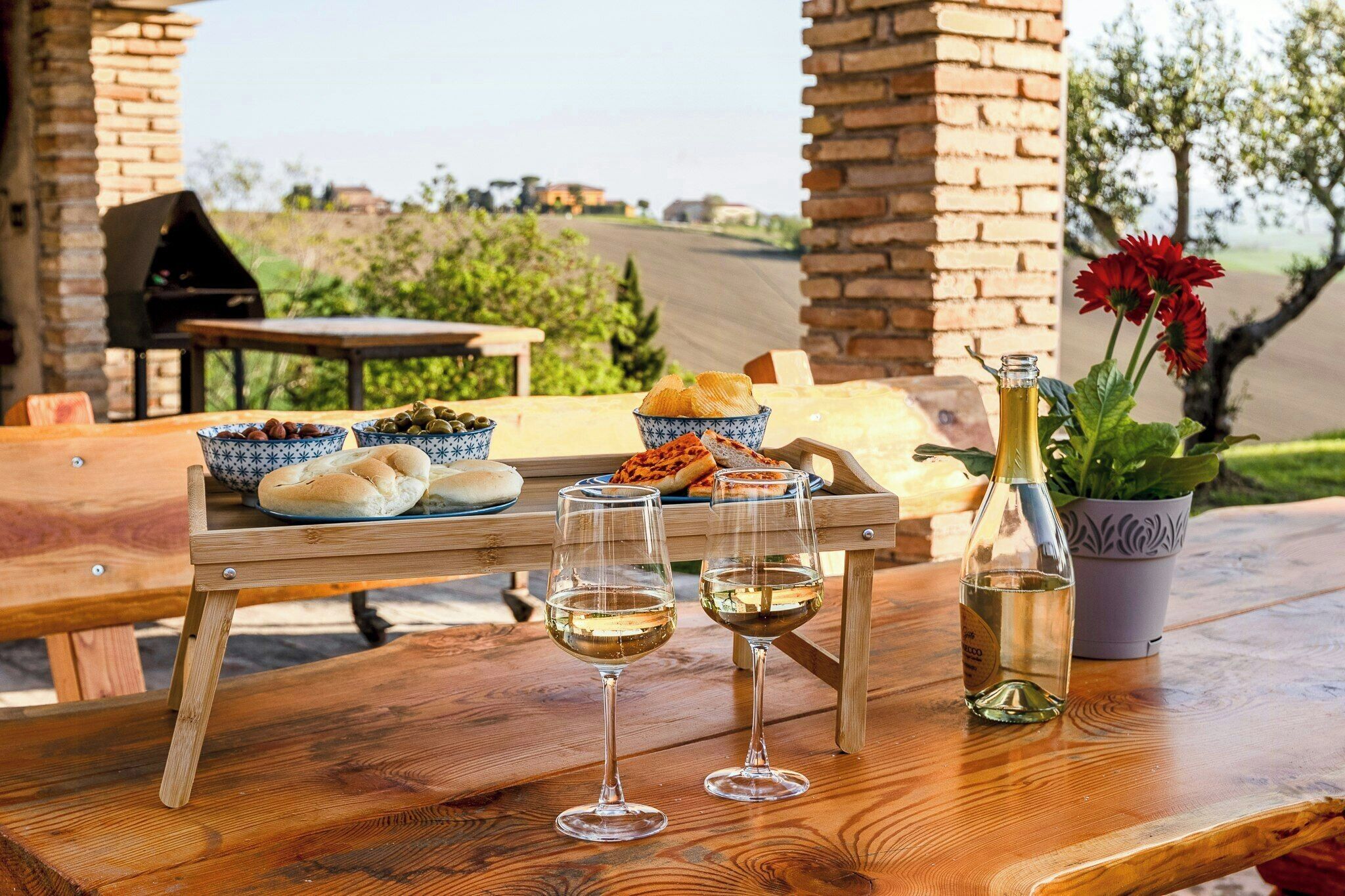 A wooden table with two wine glasses, a bottle, and bowls of olives and bread.
