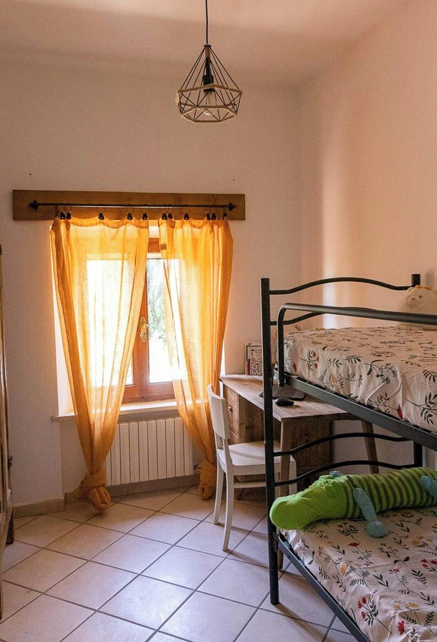 A room with a bunk bed, a desk, a chair, a radiator, and a hanging light fixture.