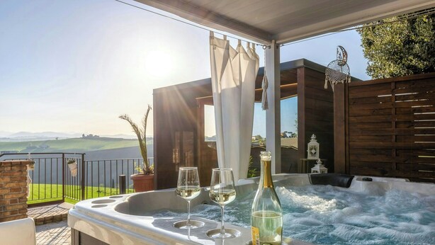Ein Whirlpool mit zwei Gläsern Weißwein und einer Flasche, ein Holzzaun und Blick auf die Landschaft.