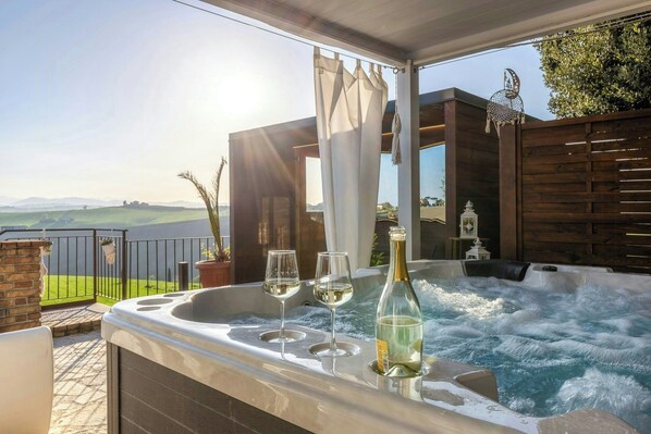 Ein Whirlpool mit zwei Gläsern Weißwein und einer Flasche, ein Holzzaun und Blick auf die Landschaft.
