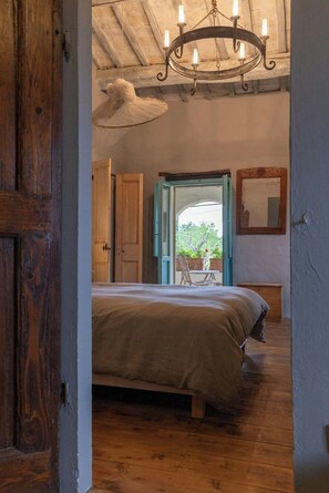 A room with a bed, wooden floor, a chandelier, and a view through an open door to an outdoor area. - Historic farmhouse with loggia in Cortona (Cortona)