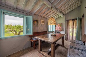 A rustic room with a wooden table, bench, and sofa, a window with a view of trees, and a hanging lamp. - Historic farmhouse with loggia in Cortona (Cortona)