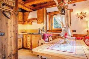 Ein rustikales Holzinterieur mit einem Esstisch, Holzschränken und einem Fenster mit Vorhängen.