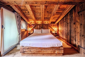 Ein Schlafzimmer einer Holzhütte mit einem Bett, zwei Nachttischen und einem Fenster mit Vorhängen.