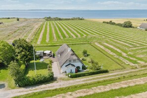 Een landelijk landschap met een huis, omringd door velden en een waterpartij in de verte.