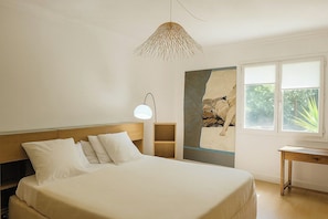 Ein Schlafzimmer mit Bett, Schreibtisch, Lampe und Fenster mit Blick auf Bäume.