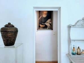 Ein Flur mit einer großen Vase auf einem Sockel, einem gerahmten Gemälde an der Wand und einem Regal mit dekorativen Flaschen.