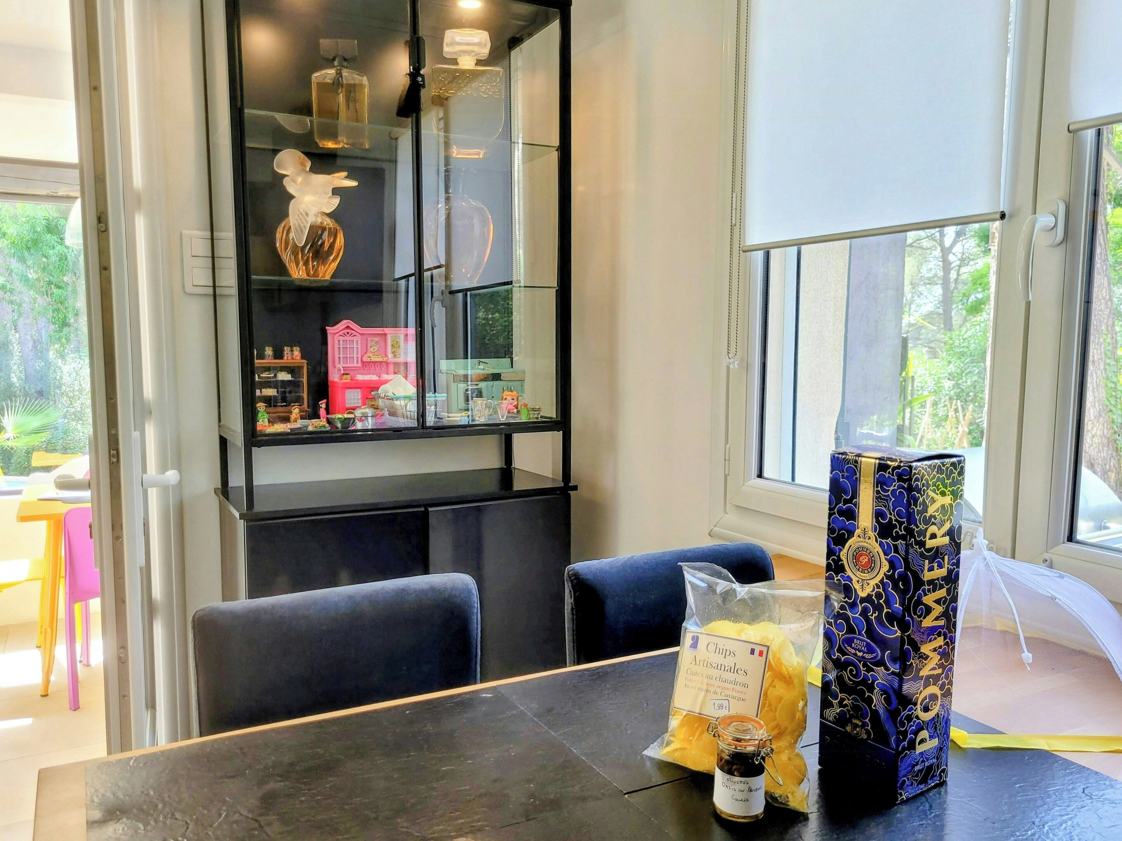 Un comedor con una mesa, sillas, un aparador de vidrio decorativo y una ventana con vista a follaje.