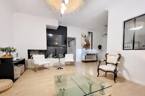 Ein modernes Wohnzimmer mit einem Glastisch, weißen Ledersesseln, einem Holzstuhl, einem Kamin und einem großen Spiegel an der Wand.