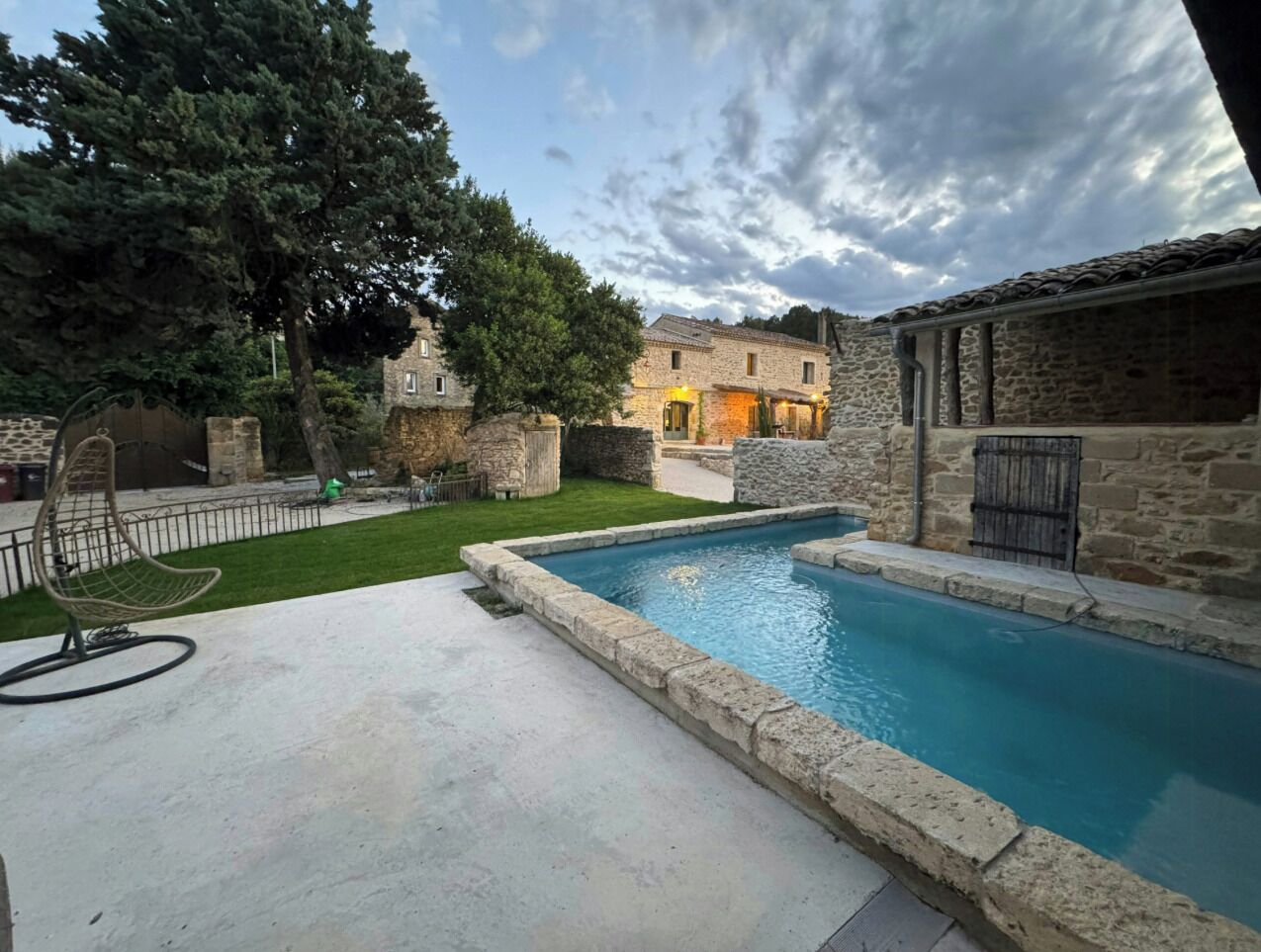A swimming pool with stone walls, a hanging chair, and a grassy area.