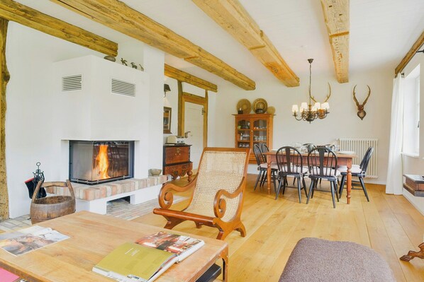 A cozy living room with a fireplace, wooden beams, a dining area, and a bookshelf. - Holiday home in rural idyll of the Uckermark (Weggun)