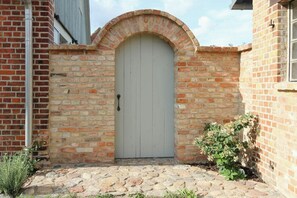 A brick building with a white door, a stone-paved entrance, and a small plant beside the door. - Holiday home in rural idyll of the Uckermark (Weggun)
