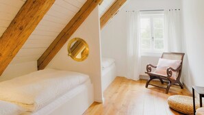 Une chambre avec un plafond en pente, un lit, une chaise, une fenêtre avec des rideaux et un miroir rond.